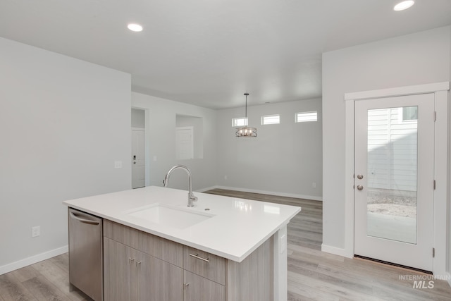 kitchen featuring baseboards, light wood finished floors, a sink, a center island with sink, and light countertops