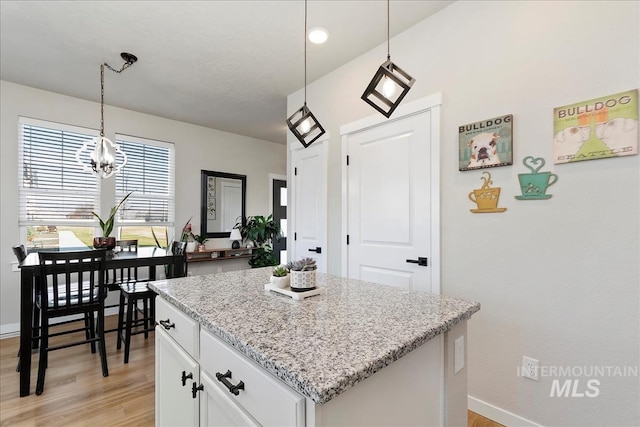 kitchen with pendant lighting, white cabinetry, a center island, light stone countertops, and light wood-type flooring