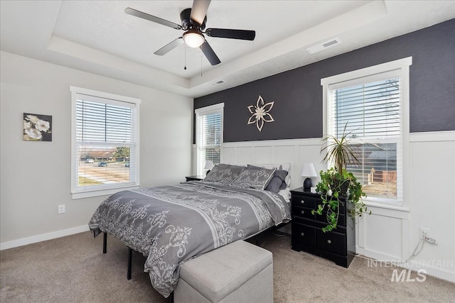 bedroom with light carpet, ceiling fan, and a tray ceiling