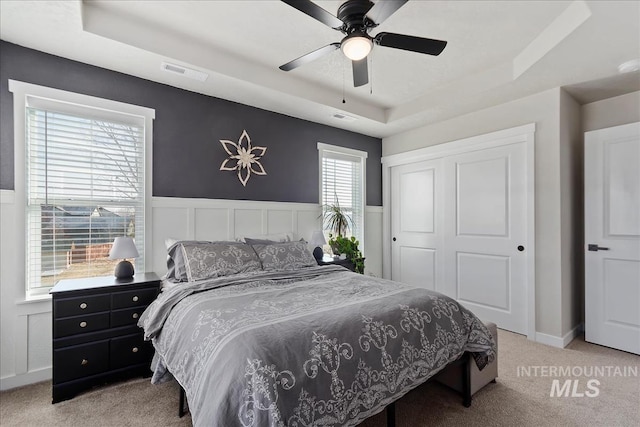 bedroom with a closet, light colored carpet, ceiling fan, and a tray ceiling