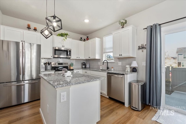 kitchen with pendant lighting, stainless steel appliances, light stone counters, white cabinets, and a kitchen island