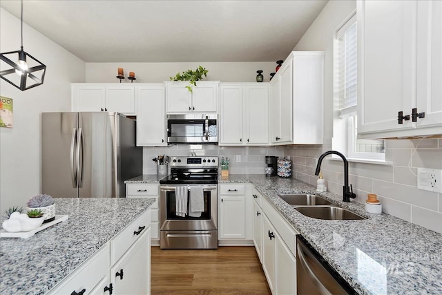 kitchen featuring sink, decorative light fixtures, stainless steel appliances, light hardwood / wood-style floors, and white cabinets