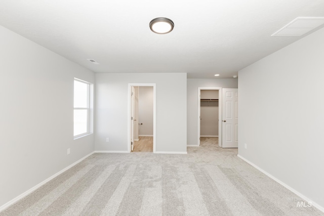 unfurnished bedroom featuring visible vents, a walk in closet, baseboards, light colored carpet, and a closet