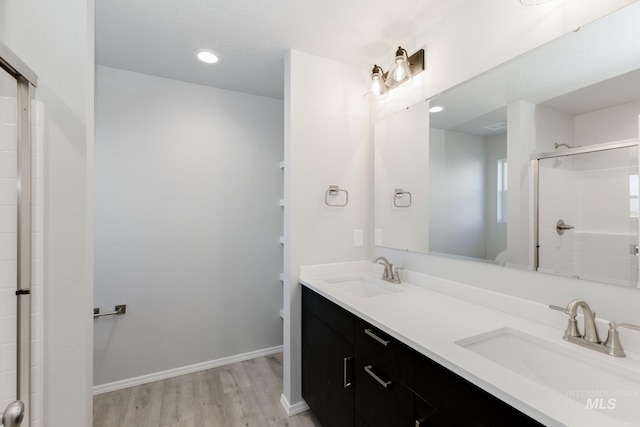 full bath featuring wood finished floors, baseboards, a tile shower, and a sink