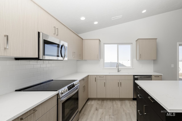 kitchen with light wood finished floors, light countertops, vaulted ceiling, appliances with stainless steel finishes, and a sink