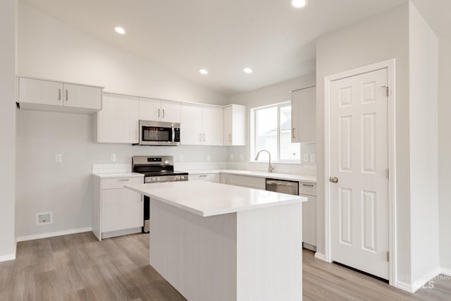 kitchen with vaulted ceiling, white cabinets, light wood-type flooring, a center island, and stainless steel appliances