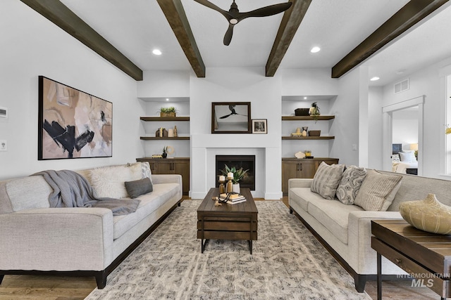 living area featuring a fireplace, a ceiling fan, visible vents, built in features, and beam ceiling