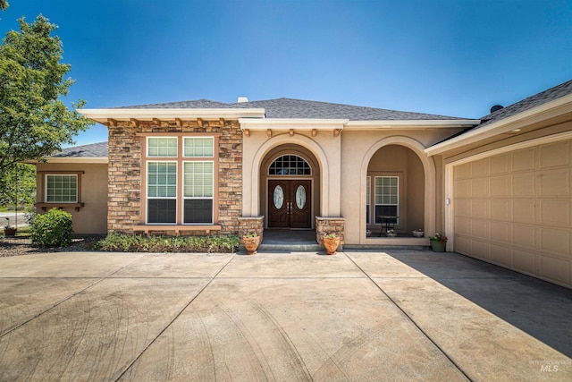 property entrance featuring an attached garage, stone siding, concrete driveway, and stucco siding