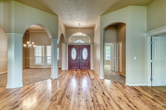 foyer entrance with a textured ceiling, light wood finished floors, an inviting chandelier, and a healthy amount of sunlight