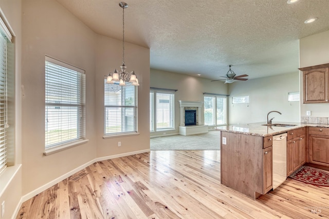 kitchen featuring a glass covered fireplace, light stone counters, a peninsula, white dishwasher, and a sink