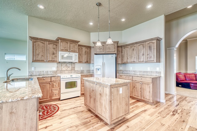 kitchen with arched walkways, decorative light fixtures, light wood-style floors, a sink, and white appliances