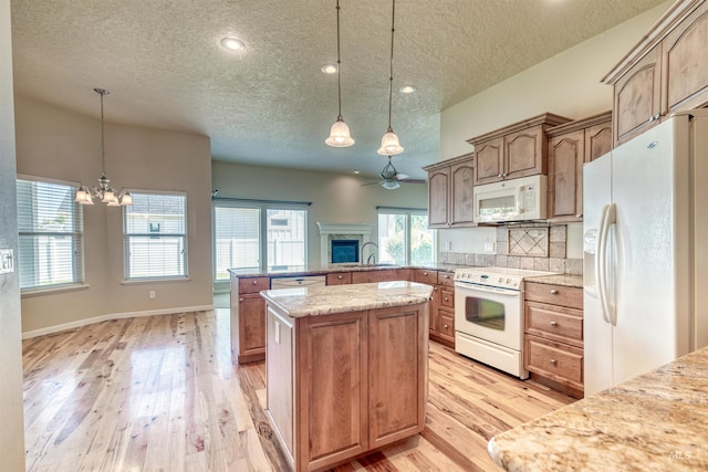 kitchen featuring white appliances, a peninsula, light wood-style floors, pendant lighting, and a sink