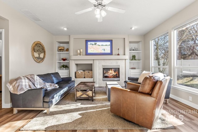 living room featuring built in shelves, a tile fireplace, light hardwood / wood-style floors, and a healthy amount of sunlight