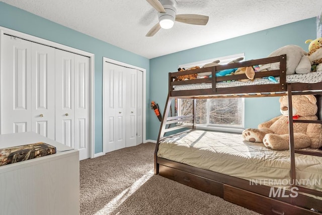 bedroom with ceiling fan, carpet flooring, a textured ceiling, and two closets