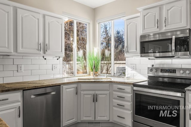 kitchen featuring dark stone countertops, tasteful backsplash, white cabinets, and appliances with stainless steel finishes