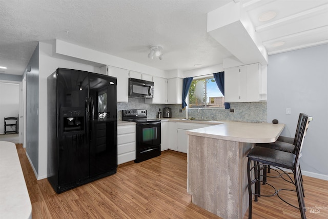 101 Patton St, Marsing, ID 83639 - kitchen featuring black appliances, a peninsula, light wood-type flooring, backsplash, and a textured ceiling