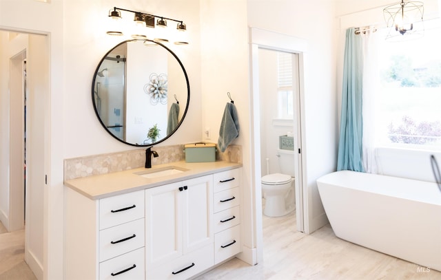 bathroom featuring a tub to relax in, an inviting chandelier, vanity, and toilet