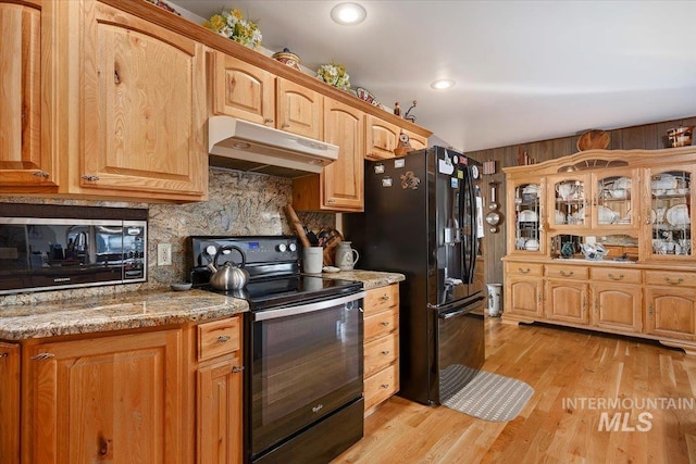 kitchen with tasteful backsplash, light stone countertops, black appliances, and light hardwood / wood-style floors