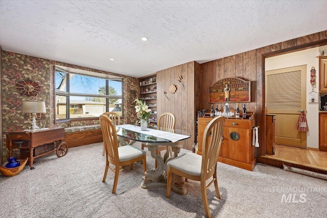 dining area with light colored carpet, wooden walls, and a textured ceiling