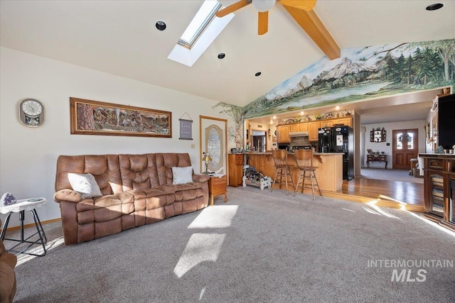 living room featuring high vaulted ceiling, a skylight, beamed ceiling, light colored carpet, and ceiling fan