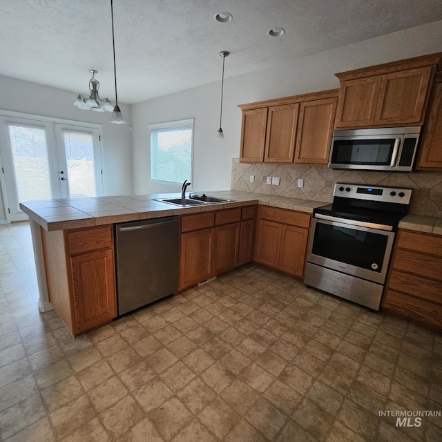 kitchen with hanging light fixtures, sink, appliances with stainless steel finishes, tasteful backsplash, and kitchen peninsula