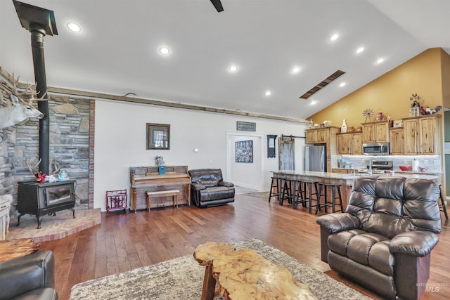 living room featuring high vaulted ceiling, hardwood / wood-style flooring, a wood stove, and recessed lighting