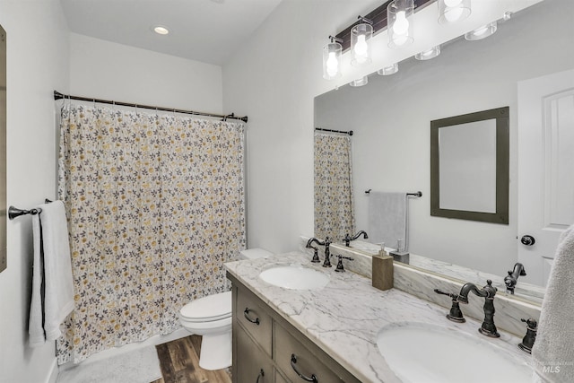 full bath featuring wood finished floors, a sink, toilet, and double vanity