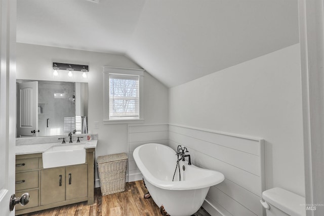 bathroom with toilet, wood finished floors, vaulted ceiling, vanity, and a freestanding tub