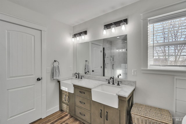 bathroom with double vanity, a stall shower, a sink, and wood finished floors