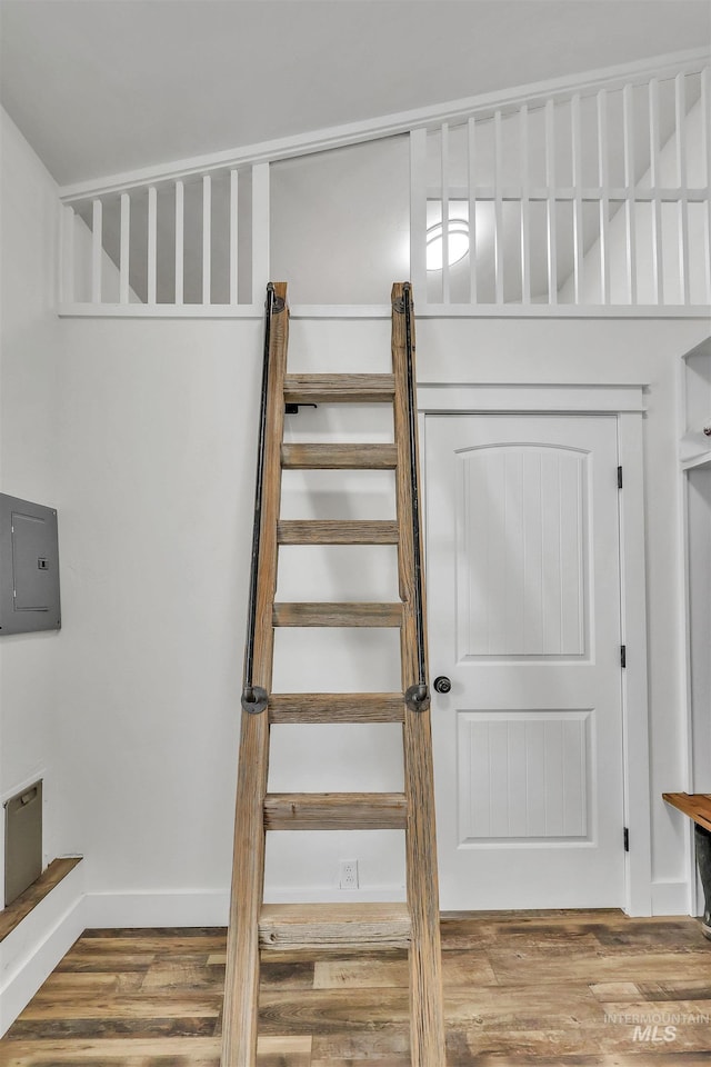 staircase with electric panel, baseboards, and wood finished floors