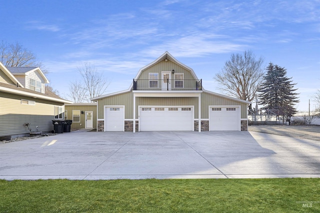 exterior space with stone siding, a gambrel roof, concrete driveway, and a balcony