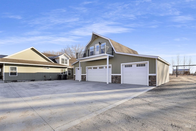 view of side of home featuring stone siding, driveway, a balcony, and a gambrel roof