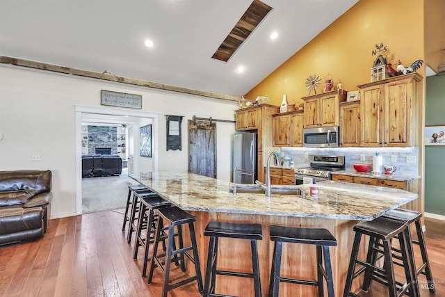 kitchen with a barn door, a sink, a kitchen breakfast bar, appliances with stainless steel finishes, and tasteful backsplash