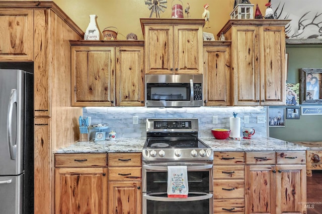 kitchen featuring stainless steel appliances, light stone counters, backsplash, and brown cabinets