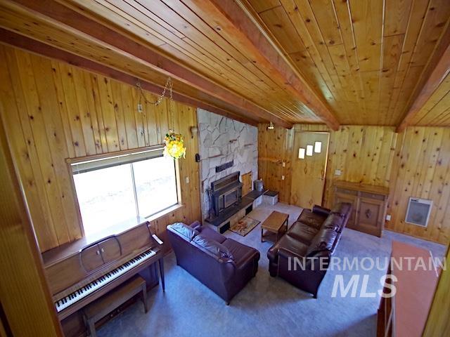 living room with wooden ceiling, beamed ceiling, wood walls, and a stone fireplace