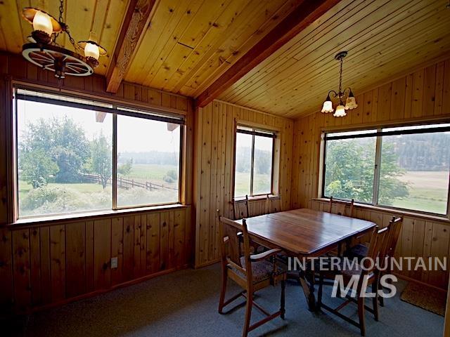 carpeted dining room featuring wooden ceiling, lofted ceiling with beams, an inviting chandelier, and wooden walls