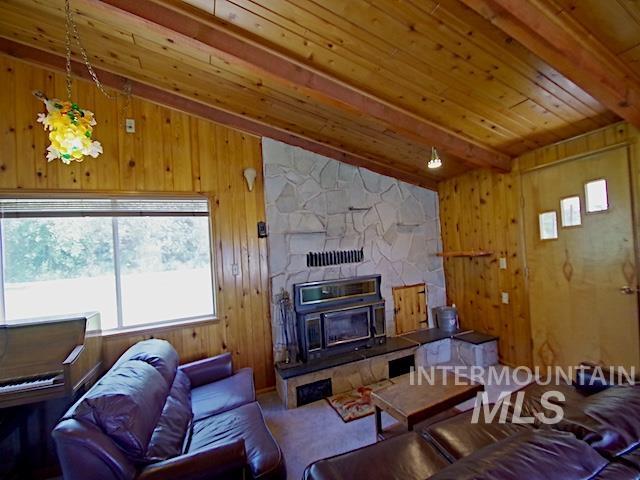 living room featuring wood ceiling, carpet floors, a stone fireplace, wood walls, and beam ceiling