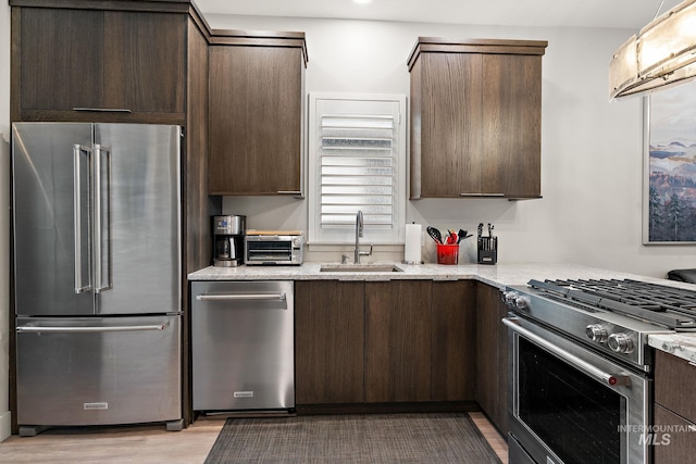 kitchen with light stone counters, a sink, high quality appliances, light wood-style floors, and dark brown cabinets