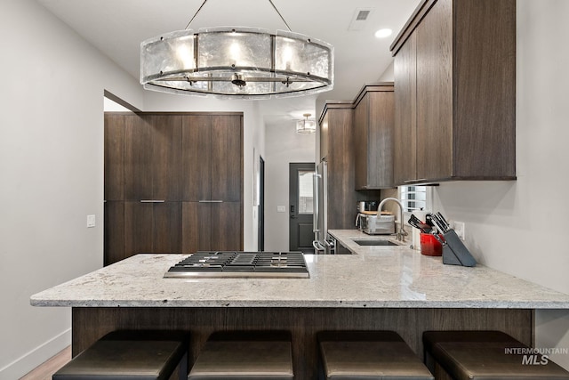 kitchen featuring baseboards, stainless steel gas stovetop, a peninsula, a kitchen bar, and a sink