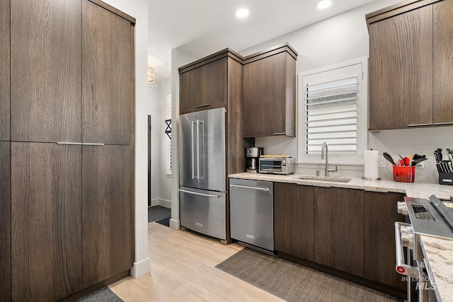 kitchen with a toaster, premium appliances, light wood-style flooring, dark brown cabinets, and a sink