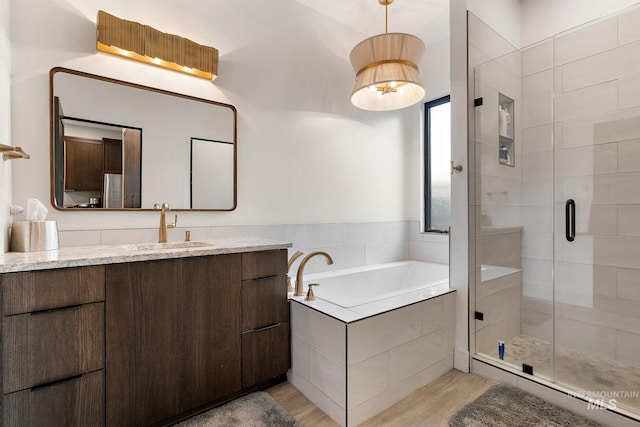 full bath featuring a stall shower, a garden tub, vanity, and wood finished floors