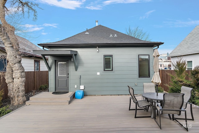 back of property with outdoor dining area, roof with shingles, fence, and a wooden deck