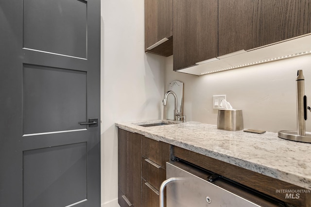 kitchen with a sink, dark brown cabinetry, and light stone countertops