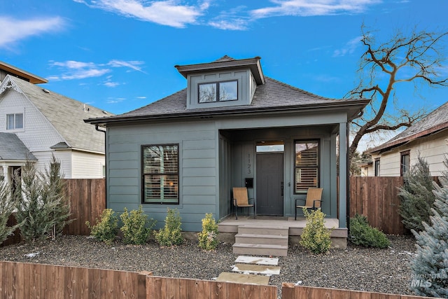 view of front of property featuring covered porch, a shingled roof, and fence