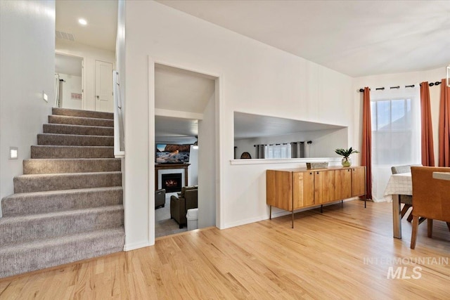 interior space with light wood-type flooring, visible vents, a lit fireplace, baseboards, and stairs