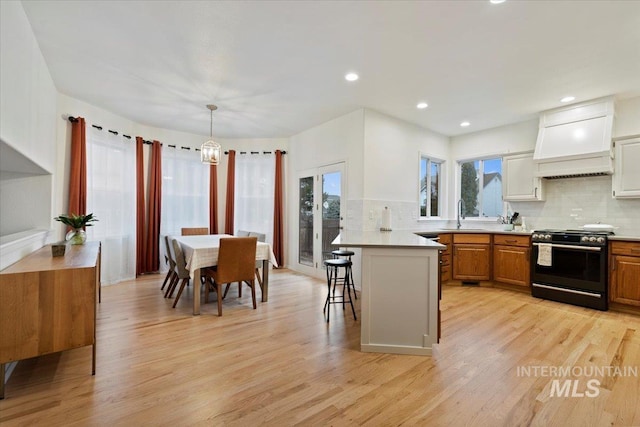 kitchen with a breakfast bar area, light wood-style flooring, custom range hood, gas range oven, and tasteful backsplash