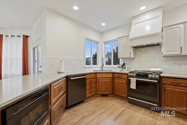 kitchen with premium range hood, a sink, light wood-style floors, gas range, and dishwasher