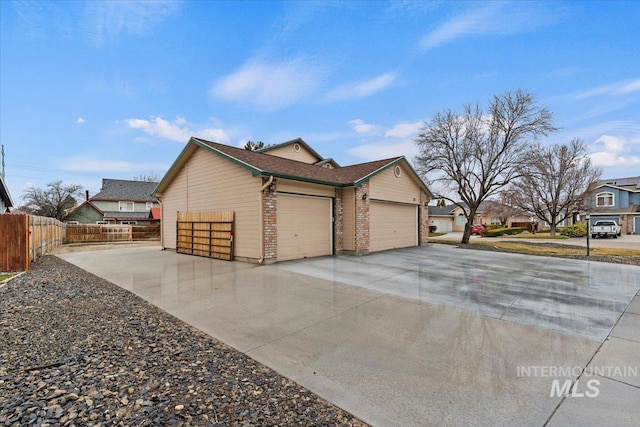 view of side of home with driveway, brick siding, an attached garage, and fence