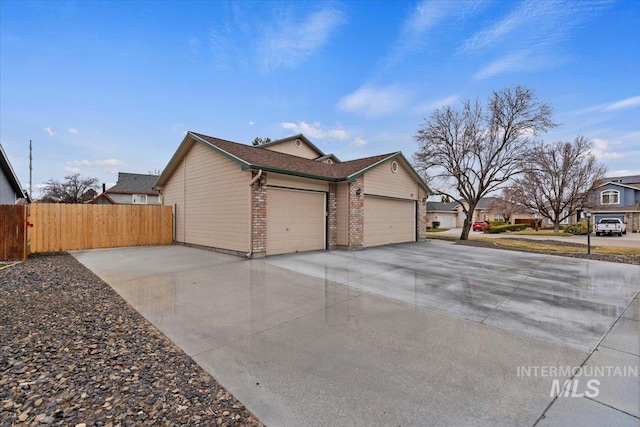 view of side of property featuring driveway, brick siding, an attached garage, and fence