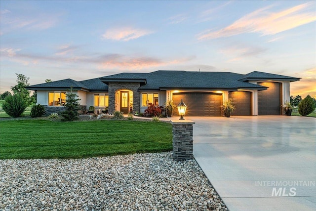 prairie-style home with driveway, a front yard, an attached garage, a shingled roof, and stone siding